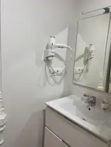 Secador de pelo blanco de pared con cable en espiral junto al espejo del lavabo, en primer plano